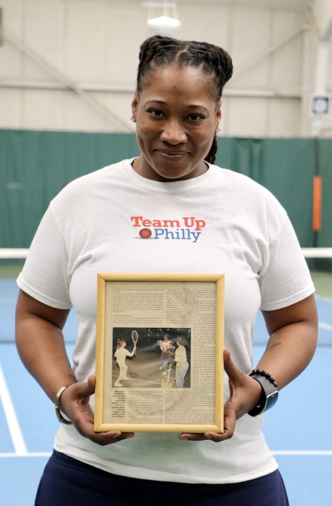 Coach Jennifer Williams holds a framed news article that includes a photo of herself as a child practicing tennis with legendary basketball player Earl Monroe.